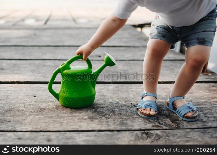 Spring and summer. Gardening. A small girl is playing with a watering can of a wooden bridge. A small girl is playing with a watering can of a wooden bridge. Spring and summer. Gardening. green watering can