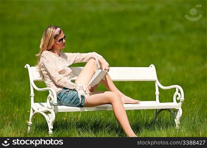 Spring and summer - Young woman relaxing in meadow on white bench on sunny day