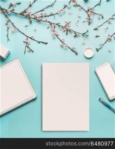 Spring background with cherry blossom twigs on blue desktop, top view, frame