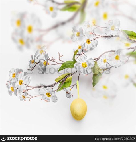 Spring blossom branches with hanging yellow Easter egg at white wall background.