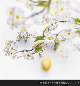 Spring blossom branches with hanging yellow Easter egg at white wall background.
