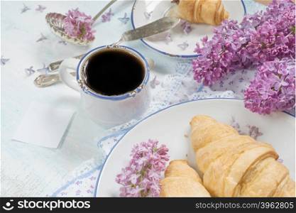 Spring breakfast with a cup of black coffee, croissants and lilac flowers