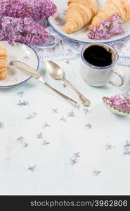 Spring breakfast with a cup of black coffee, croissants and lilac flowers