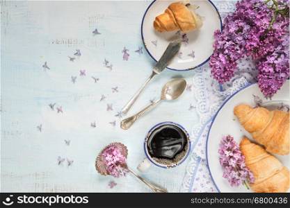 Spring breakfast with a cup of black coffee, croissants and lilac flowers, with space for text