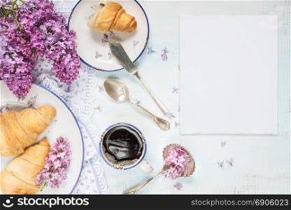 Spring breakfast with a cup of black coffee, croissants, white blank paper card and lilac flowers, with space for text