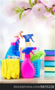 Spring cleaning concept - colorful spays and rubbers on wooden table over spring background. Spring cleaning concept