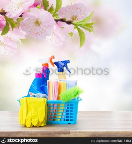 Spring cleaning concept - colorful spays and rubbers on wooden table with spring background. Spring cleaning concept