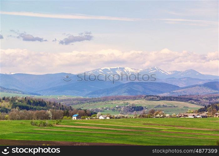 Spring fields and orchard blossom on foothills. Sunny green spring landscape. Spring fields and blooming trees. Village and town behind foothills
