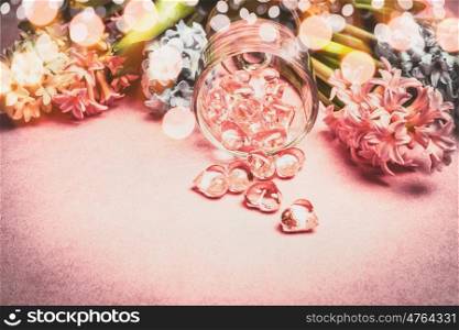 Spring flowers border with bokeh and glass hearts decoration on pink background