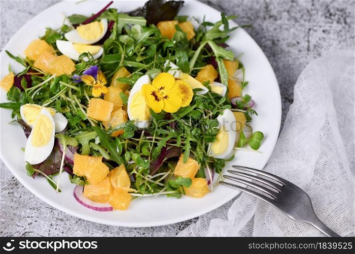 Spring fruit, citrus and vegetable salad from a mix of lettuce leaves and sprouts of radish and lentils, arugula, microgreens, quail egg wedges, with edible flowers - pansies