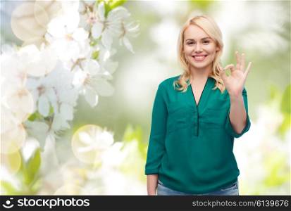 spring, gesture, plus size and people concept - smiling young woman in shirt and jeans showing ok hand sign over natural cherry blossom background