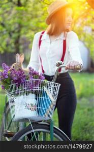 spring in the village. girl with a bicycle on a walk and a bouquet of lilacs with a rabbit in a bicycle basket. spring mood