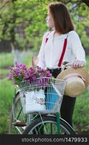 spring in the village. girl with a bicycle on a walk and a bouquet of lilacs with a rabbit in a bicycle basket. spring mood