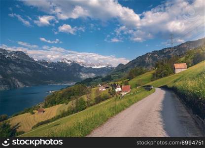 Spring landscape with country road toward a village, near Walensee lake and the Alps mountains, under blue sky, in St. Gallon Canton, Switzerland.
