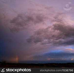 Spring meadow after rain, cloudy evening pre sunset sky with rainbow, rural hills and fields in far. Natural seasonal, weather, climate, countryside beauty concept scene.