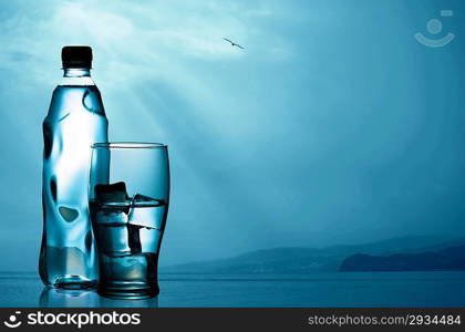 Spring mineral water bottled with glass and ice against natural marine landscape