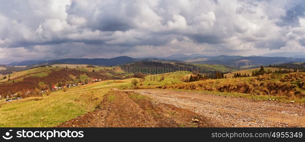 Spring mountain panorama. Clouds and sun on the hills. Spring storm. April rain. Village in the valley. April rural scene