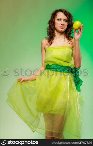 Spring or summer food concept. Portrait of curly girl young woman in green dress holding apple fruit on green. Studio shot.