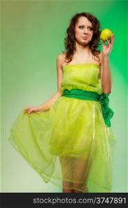 Spring or summer food concept. Portrait of curly girl young woman in green dress holding apple fruit on green. Studio shot.
