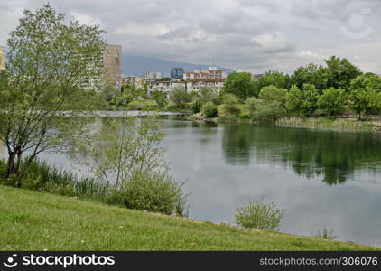 Spring panorama of a part of residential district neighborhood along a lake with green trees, shrubs and flowers, Drujba, Sofia, Bulgaria