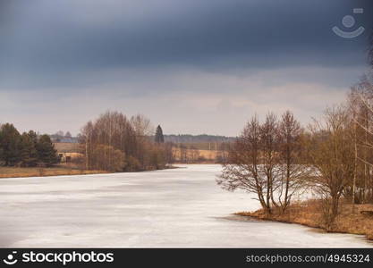 Spring rural scene. Lake under ice and snow melting. Cloudy spring day. Early spring. Mud season.