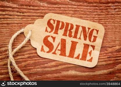 spring sale sign - red stencil text on a paper price tag against grunge wood