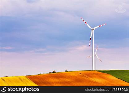 Spring sunny day, green fields with wind power generators. Eco power. Wind turbines park generating electricity. Hunting box on top of the hill. Lower Austria near Poysdorf.