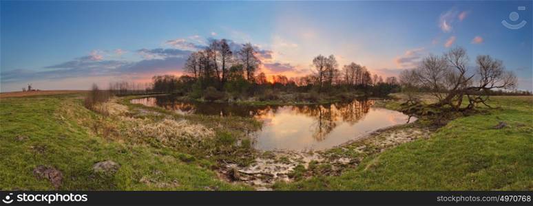 Spring sunset panorama. Small river in evening light. Rural scene.