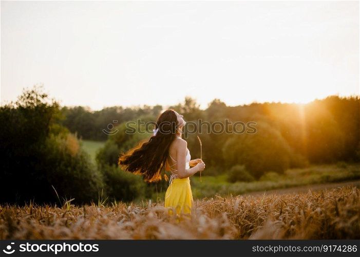 spring, sunset, wheat field, girl, evening, sun, yellow skirt, white t-shirt, white bow, hand with a spike, rustic style, girl&rsquo;s smile, bread field, model, contour light. A girl in a yellow skirt stands in a field against the background of the setting sun