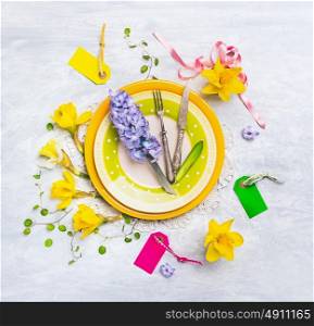 Spring table decoration with with narcissus , hyacinths , sign, ribbons , knife and fork on green plate , top view