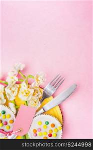 Spring table place setting with plate, cutlery , Narcissus flowers bunch, cake and blank tag on pastel pink background, top view, place for text