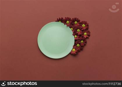 Spring table settings with green empty dish and red flowers ornament, on a red background. Eco-friendly empty platter. Minimal food background.