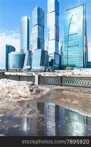 spring urban landscape with view of Moscow City and melting snow puddle