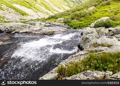 Spring waterfall in mountain valley. Fast river with green shores