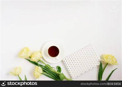 Spring yellow tulips, coffee mug, notebook on a white background. Flat position, top view.