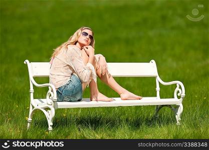Spring - Young woman relaxing on bench in meadow on sunny day