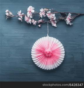 Springtime decoration with artificial spring blossom twig and pink party paper fan on gray blue background, top view