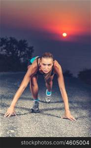 Sprinter woman on the start, preparing to run, training for athletic competition, evening workout outdoors over beautiful sunset background, the concept of hard work and willpower. Sprinter woman on the start
