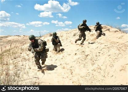 Squad of soldiers run through the desert through the military operation