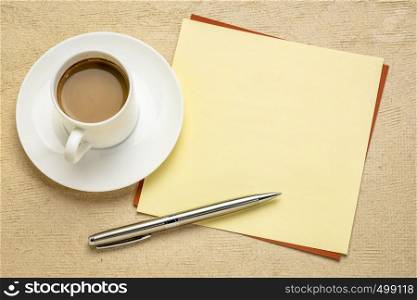 square blank yellow note with a cup of coffee and pen against textured paper