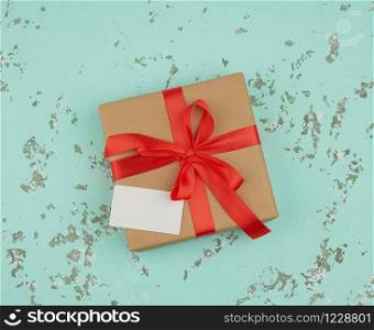 square box wrapped in brown kraft paper and tied with a red silk ribbon, on top of an empty white business card, green background