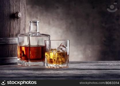 Square decanter and a glass of whiskey with ice on background barrel. Square decanter and a glass of whiskey with ice