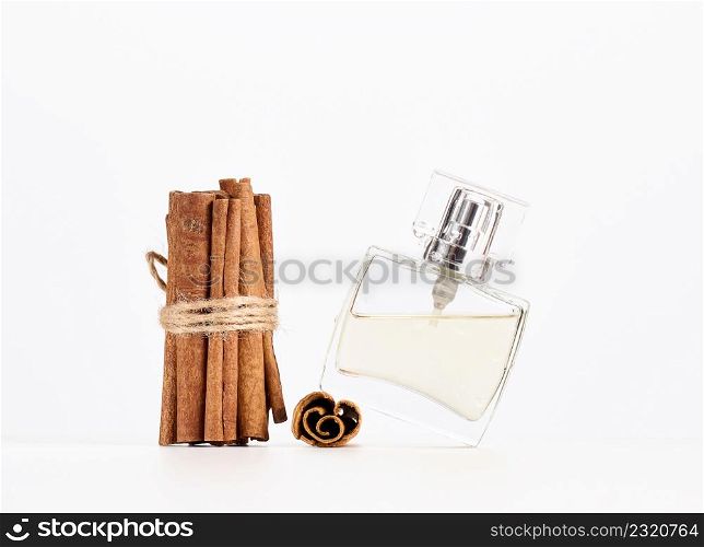 square glass perfume bottle on white background and a bunch of cinnamon