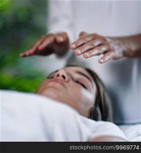 Square image of Reiki therapist holding hands above head of the patient and transfer energy. Peaceful teenage girl lying with her eyes closed. 