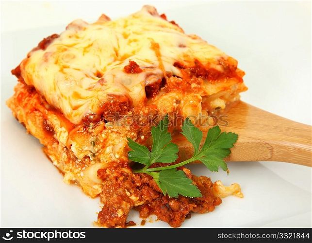 Square of baked lasagna with parsley on bamboo serving spoon