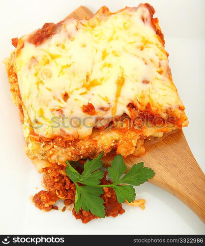 Square of baked lasagna with parsley on bamboo serving spoon