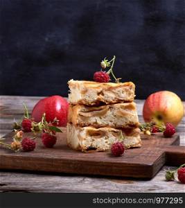 square pieces of apple pie are stacked on a brown wooden board, sponge cake