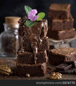 Square pieces of chocolate cake are covered with a thick layer of chocolate, close up