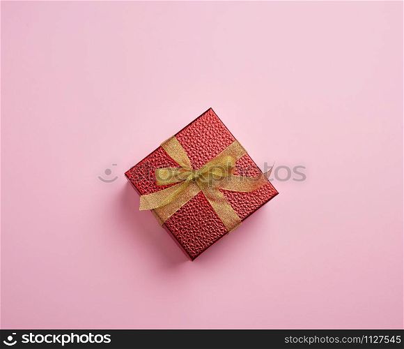 square red box tied with a golden ribbon, concept of congratulations and gifts, top view, pink background