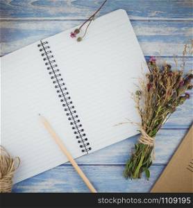 Square Top view of autumn dry flowers with grass background over blue toned wooden table with notebook mock up and copy space in rustic style, template for text